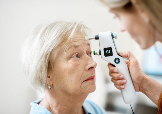 Glaucoma-scaled Female ophthalmologist measuring the eye pressure with modern tonometer to a senior patient in the medical office, close-up view
